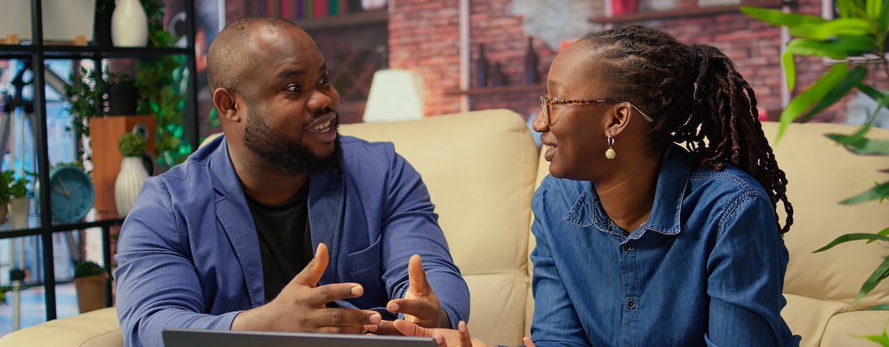 African american young freelancers on couch sharing a business idea, using modern technology and tools to analyze trends and boost success. Couple improving workflow efficiently. Camera A.